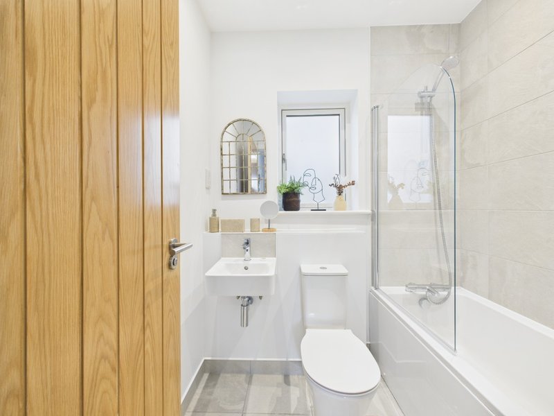 Modern bathroom with wooden door, white sink, toilet, bathtub with glass screen and wall mirror