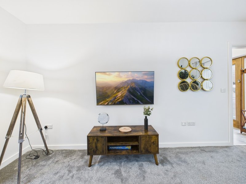 Bright living room with TV on wood stand, tripod lamp, wall art, and decorative baskets