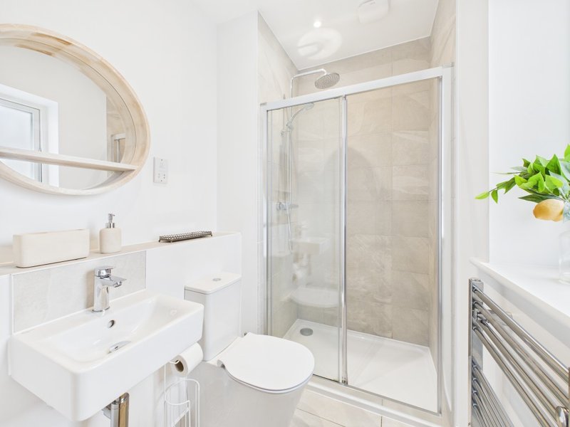 Modern bathroom with white sink, toilet, glass shower enclosure and round mirror