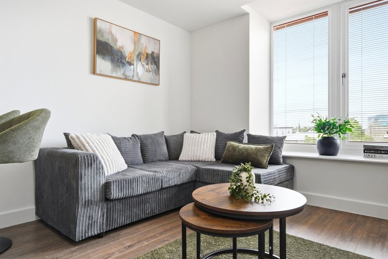 Modern living room with gray corner sofa, wooden coffee table, framed artwork and windows