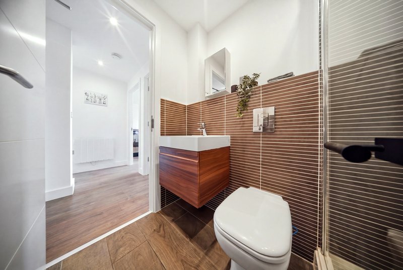 Modern bathroom with wooden vanity, white sink, toilet, wooden floor and horizontal wood-panelled walls
