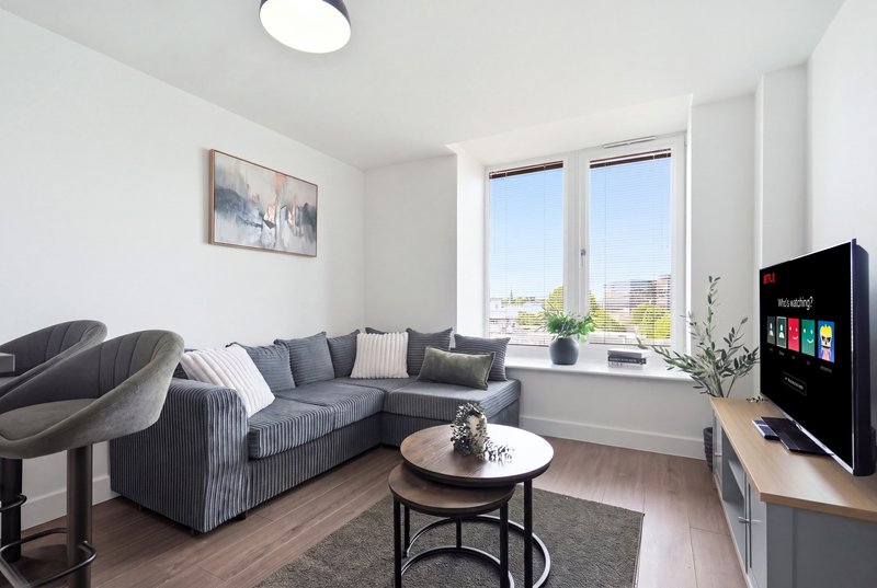 Modern living room with grey corner sofa, round coffee table, smart TV and large windows with city views