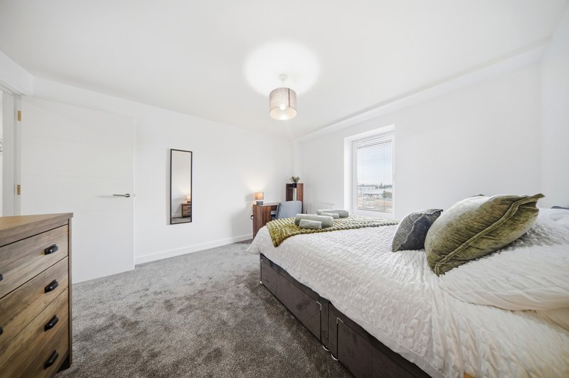 Bright modern bedroom with double bed, wooden dresser, mirror and ceiling light