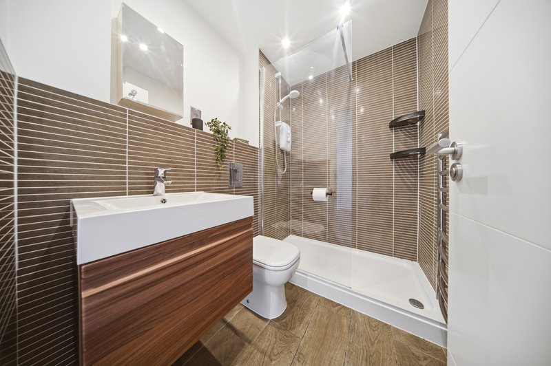 Modern bathroom with white sink, wooden vanity, walk-in shower and toilet