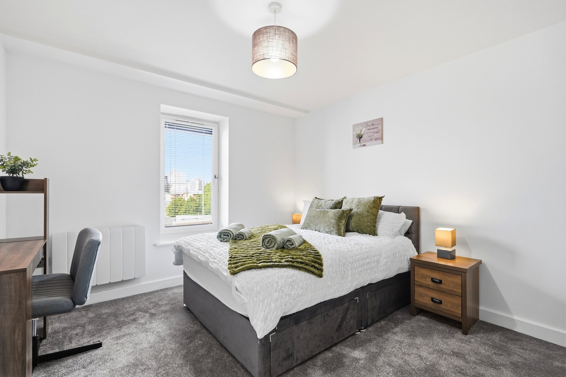 Bright bedroom with double bed, green cushions, wooden nightstand and desk area by window