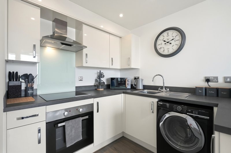 Modern kitchen with white cabinets, black countertops, built-in oven, washing machine and wall clock