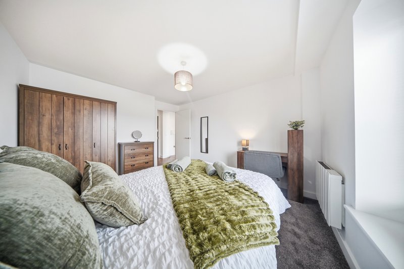 Bedroom with double bed, green and grey bedding, wooden wardrobes and dark carpet flooring