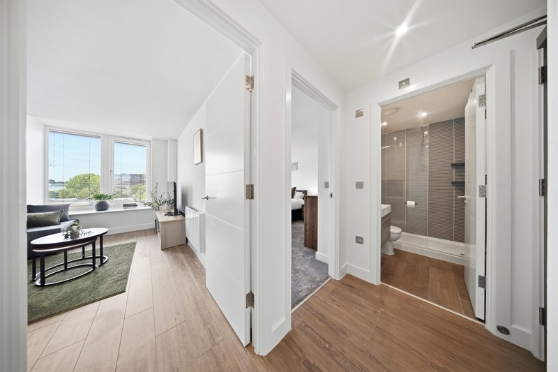 Bright hallway with white doors, wood flooring, leading to bedroom and bathroom areas