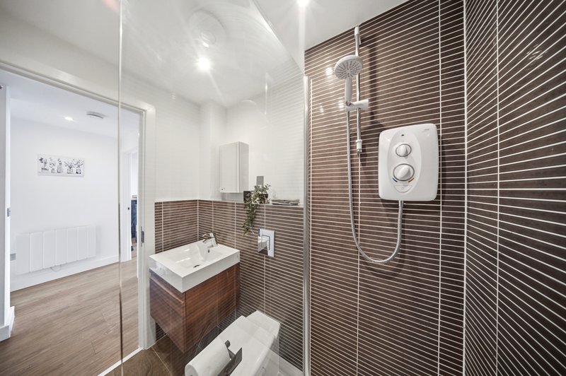 Modern bathroom with brown tile shower, wooden vanity, white sink and toilet
