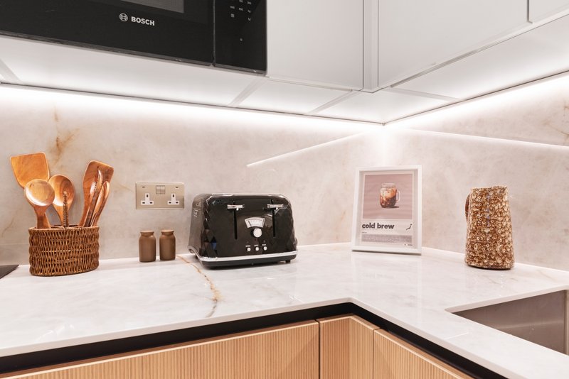Modern kitchen with white countertop, wooden cabinetry, Bosch microwave, and decorative items