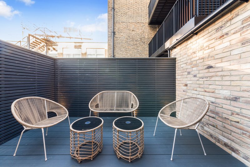 Modern rooftop terrace with three woven chairs and two round side tables
