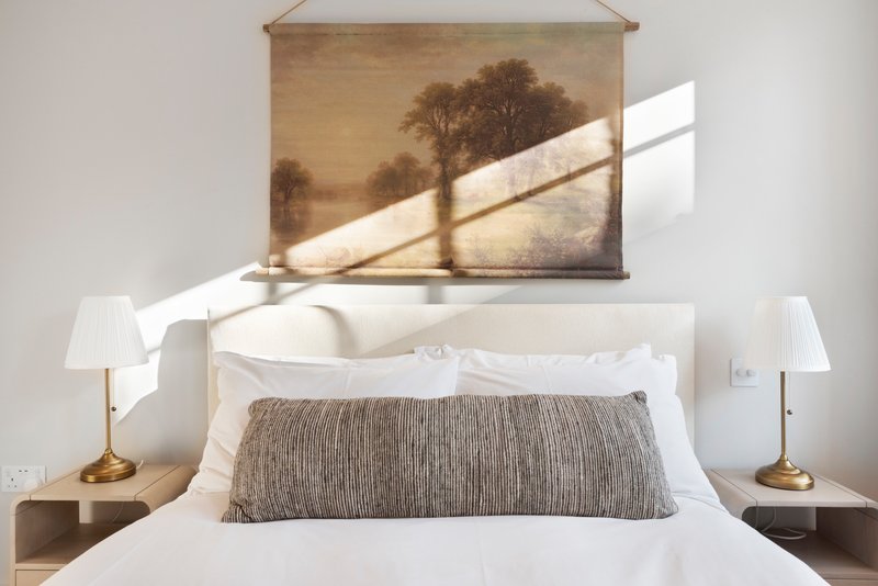 Bedroom with white bedding, grey textured pillow, wall art, and brass bedside lamps