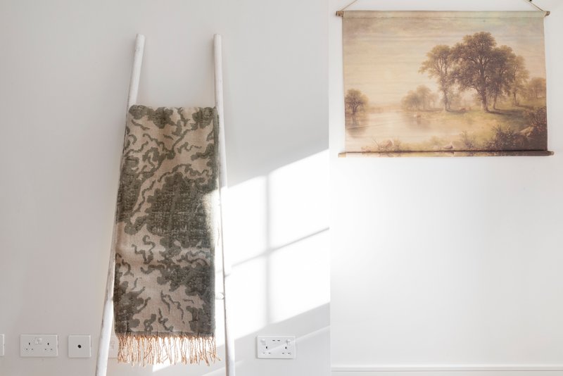 Bright room with decorative fabric throw on wooden ladder and landscape wall art