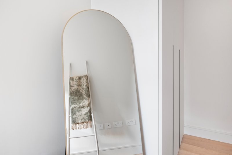Modern bedroom with tall arched mirror, decorative towel, and wooden flooring