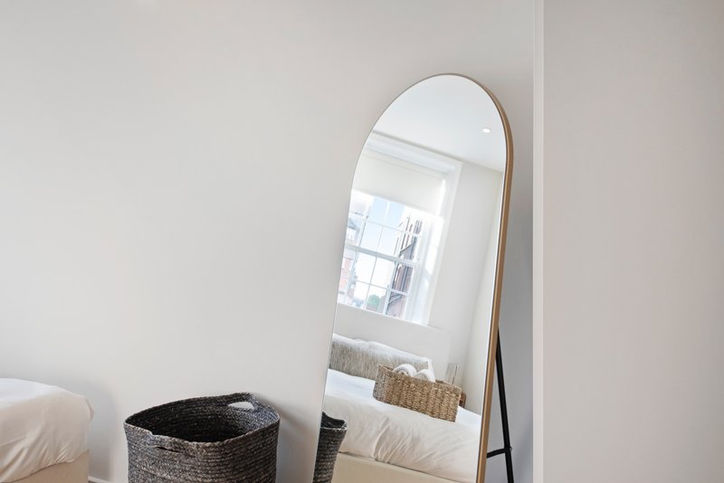 Bright bedroom corner with standing mirror, woven storage basket and white bedding