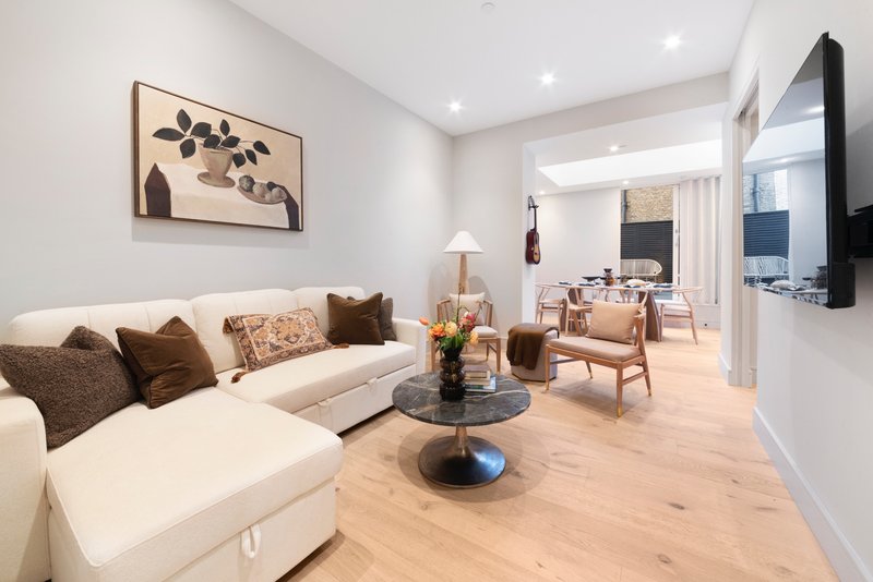 Modern living room with cream sectional sofa, wooden coffee table, framed wall art, and light wood flooring