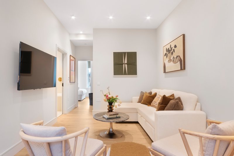 Modern living room with cream sofa, wooden chairs, wall art, and mounted television