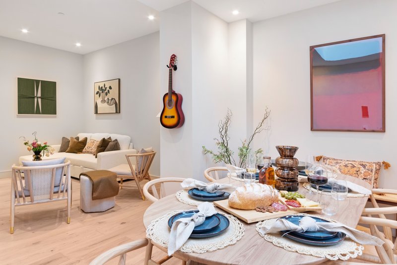 Open-plan living and dining area with wooden furniture, set dining table, and wall art including guitar