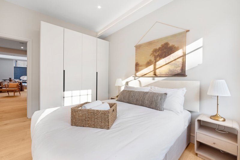 Modern bedroom with white bed, woven basket, framed landscape artwork and wooden flooring