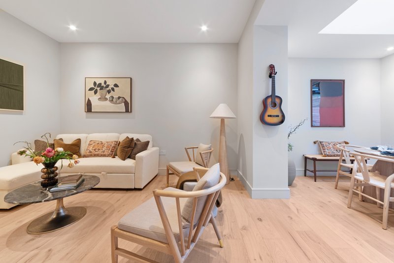 Open-plan living space with cream sofa, wooden furniture, guitar on wall, and modern lighting