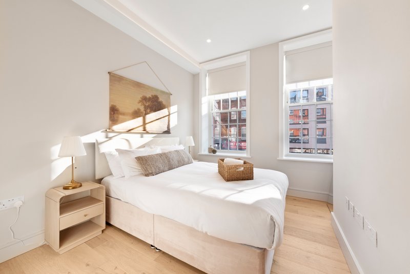 Bright modern bedroom with double bed, wooden nightstand, wall art and large windows