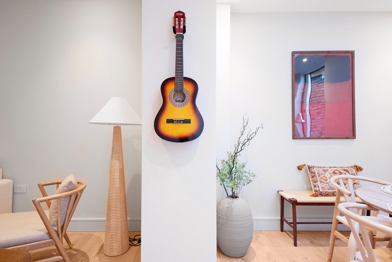 Bright living room with wooden furniture, acoustic guitar on wall, lamp, and decorative items