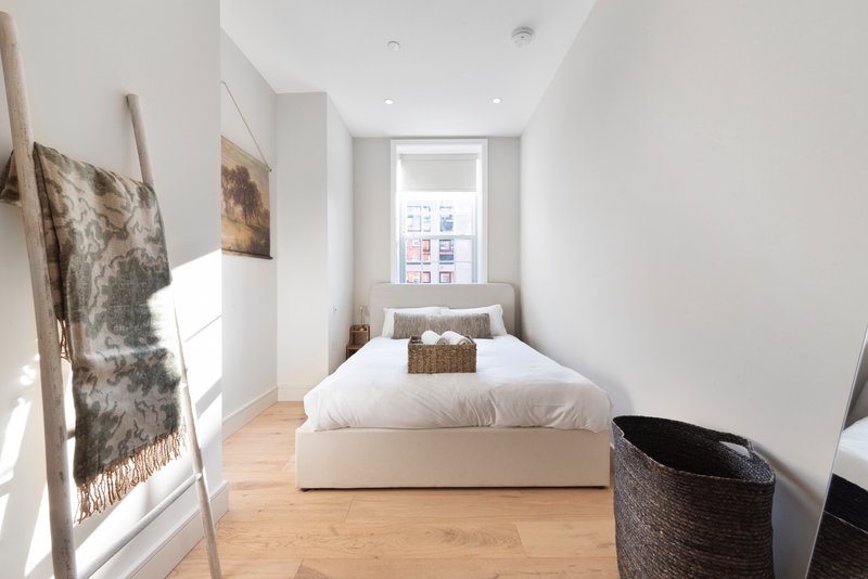 Narrow bedroom with single bed, wooden floor, window and woven storage basket