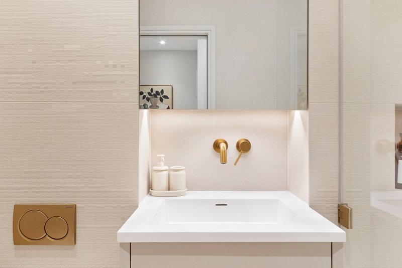 Modern bathroom sink with mirror, brass faucet, white toiletries and beige wall