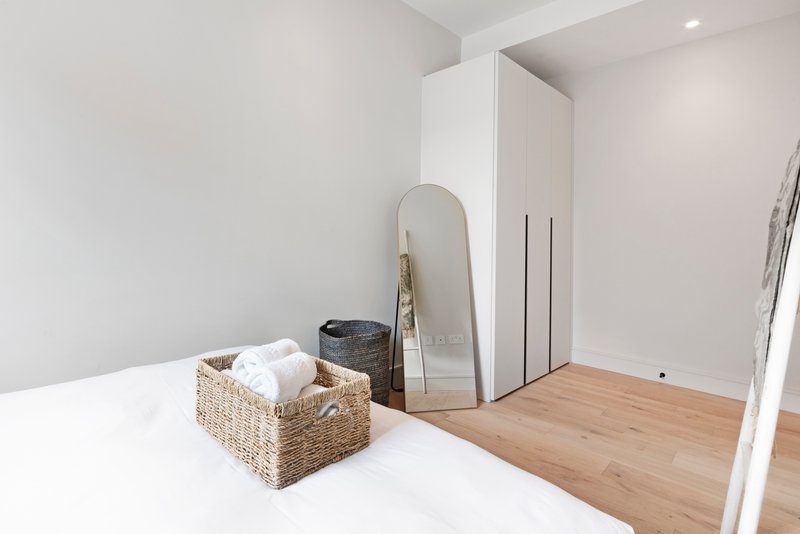 Bright bedroom with white bed, woven storage basket, round mirror, and wooden flooring