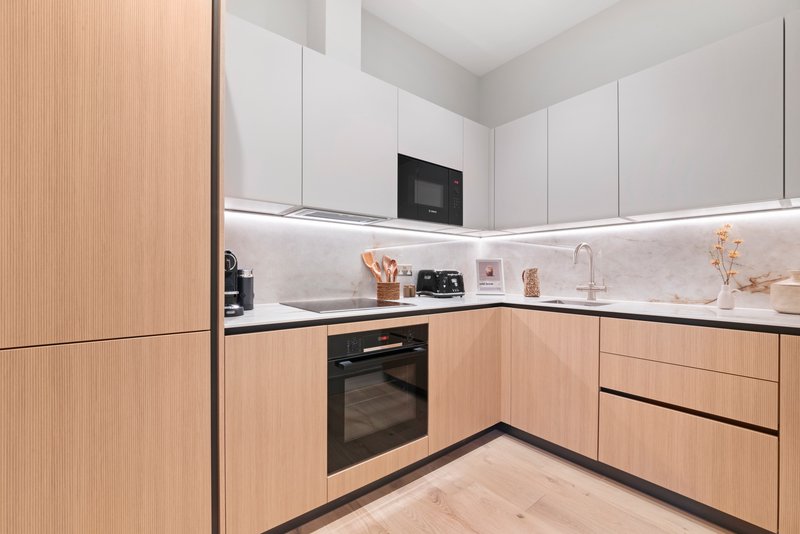 Modern kitchen with light wood cabinetry, white countertop, integrated black oven and microwave
