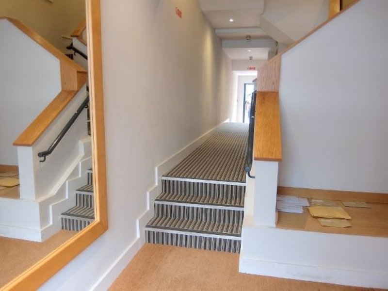 Wooden staircase with gray striped runner and white walls, natural light from entrance ahead