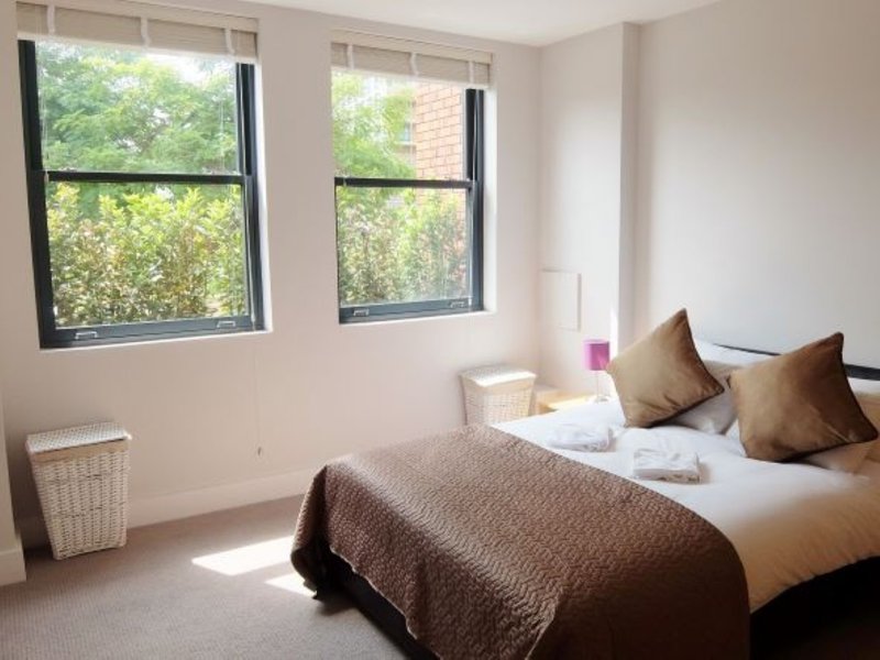 Bright bedroom with double bed, brown bedding, two windows with green views, and cushions
