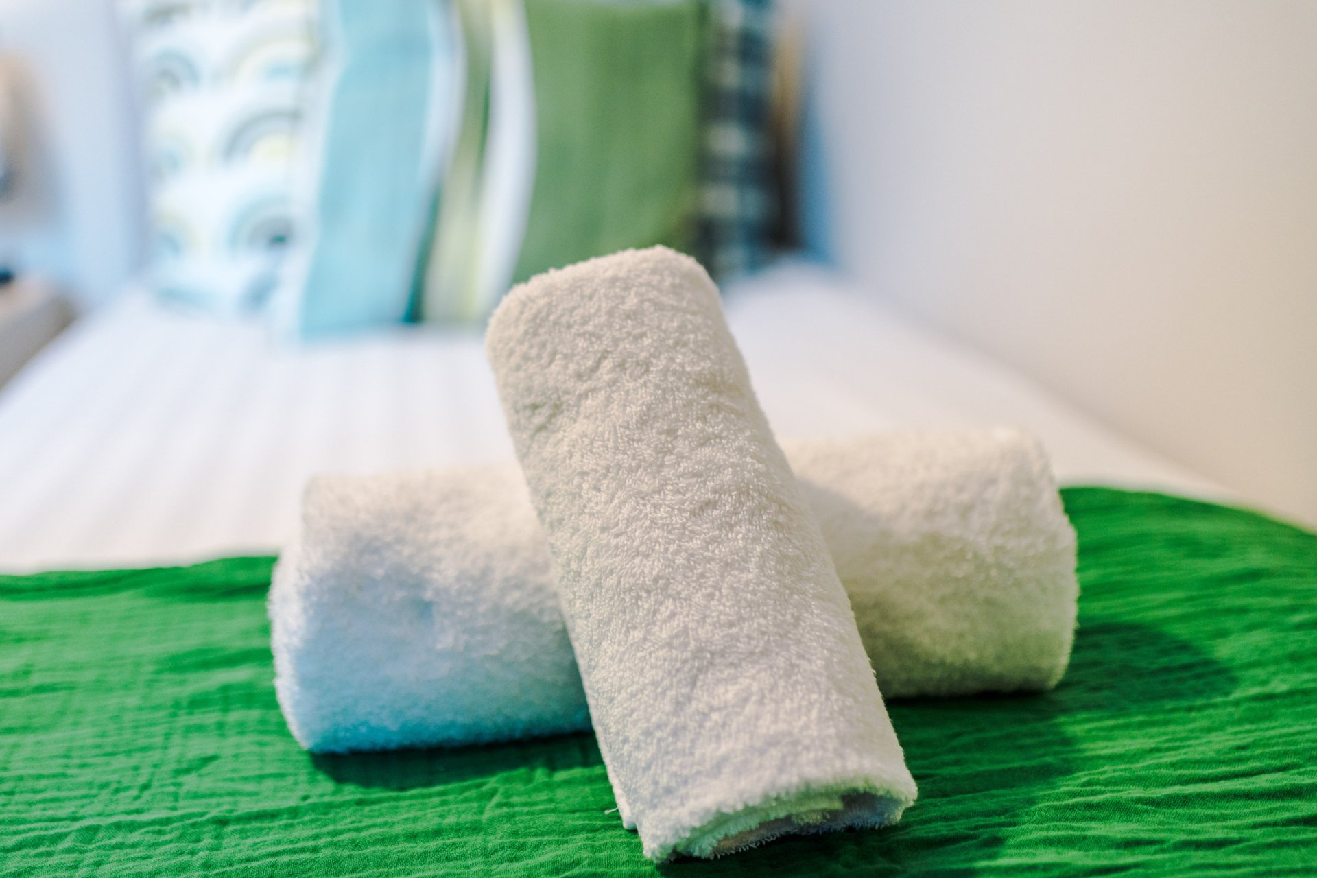 Rolled white towels arranged on green surface, bathroom amenities detail