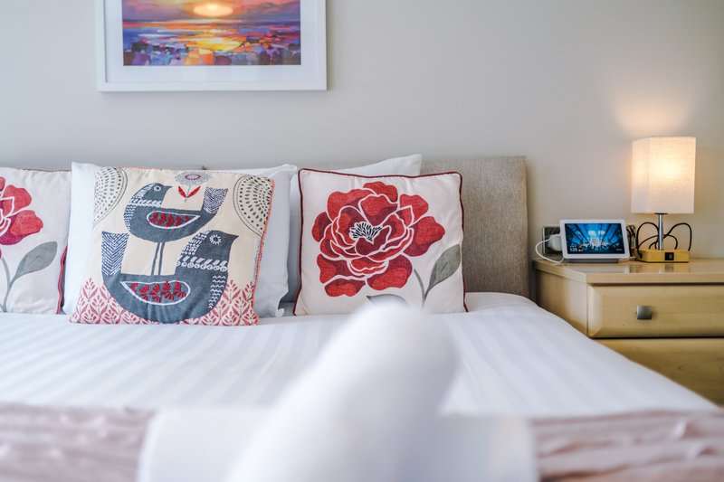 Bedroom with double bed, patterned cushions, wooden bedside table and framed sunset artwork