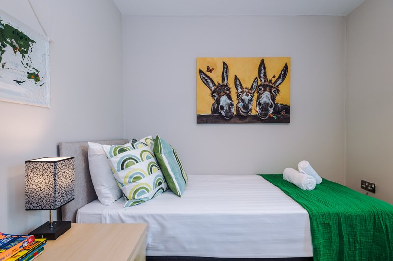 Bright bedroom with single bed, green throw, patterned cushions, bedside lamp and wall art