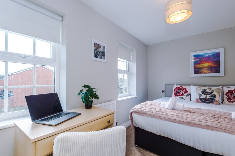 Bright bedroom with double bed, wooden desk, laptop, potted plant and framed artwork