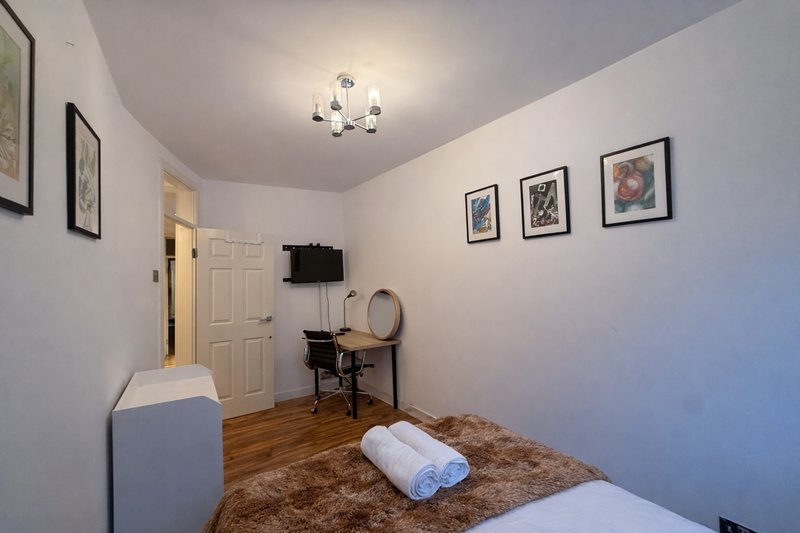 Bedroom with white walls, wooden floor, bed, desk, chair and wall-mounted framed artwork