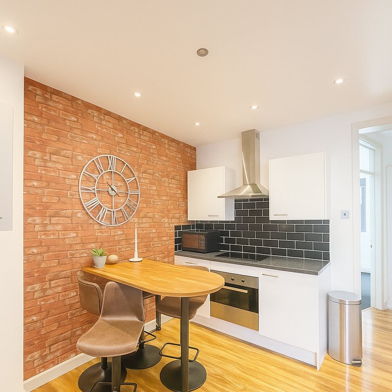 Modern kitchen with brick accent wall, white cabinetry, black tile backsplash and dining table