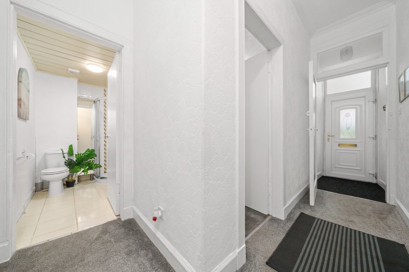 Bright hallway with white walls, beige tile flooring, mirrors, potted plant and entrance door