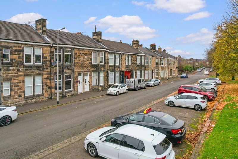 Row of stone terraced houses with street frontage, parked cars and green verge