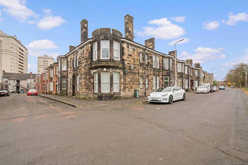Stone corner building with white car parked on street, clear blue sky