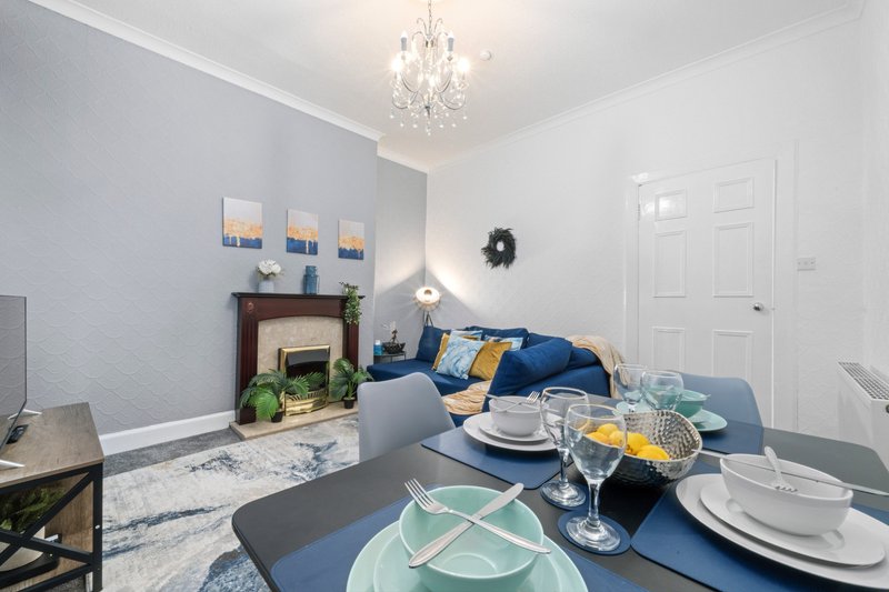 Modern living room with dining table, blue sofa, fireplace, and crystal chandelier