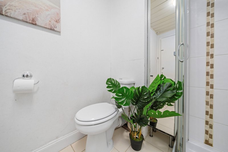 Bathroom with toilet, shower enclosure, green plant in vase, and tiled walls