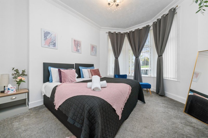 Bright bedroom with double bed, pink and black bedding, large windows with curtains, and wooden furniture