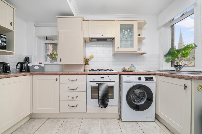 Modern cream kitchen with white subway tiles, gas hob, washing machine, and potted plants by window
