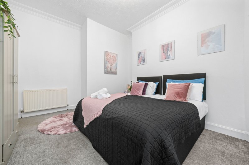 Modern bedroom with black bed, pink bedding, framed artwork, radiator and carpet flooring