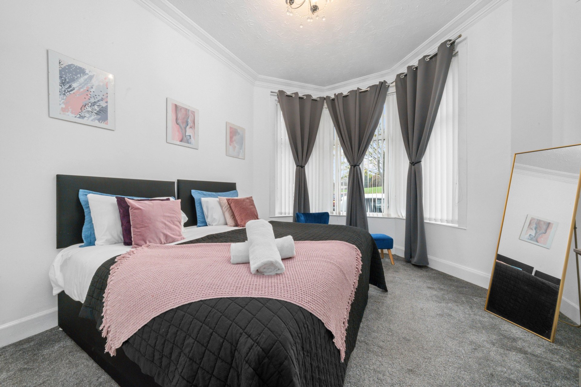 Bright modern bedroom with black bed, pink bedding, bay windows with grey curtains