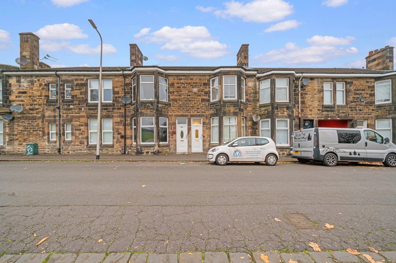 Stone terraced building with multiple doors and windows, parked vehicles in front