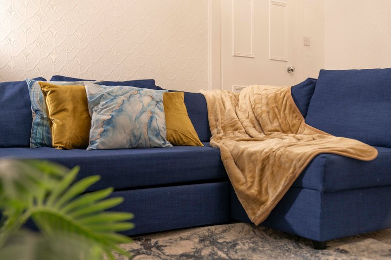 Blue sectional sofa with decorative cushions and tan throw blanket in living room