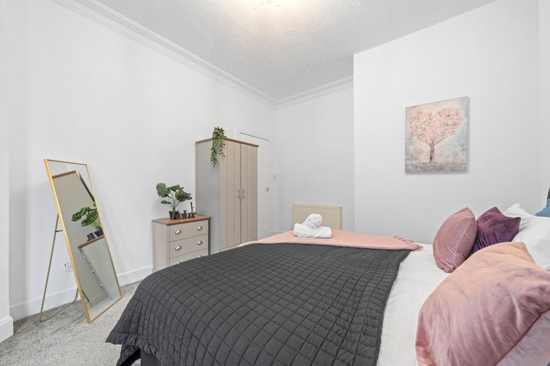 Bright bedroom with double bed, pink pillows, wooden furniture, mirror and wall art
